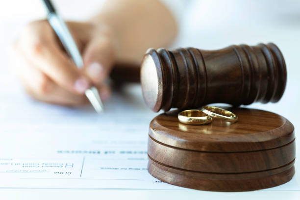 Weeding rings and  gavel with a person signing a contract in the background. Representing justice steps of divorce process.