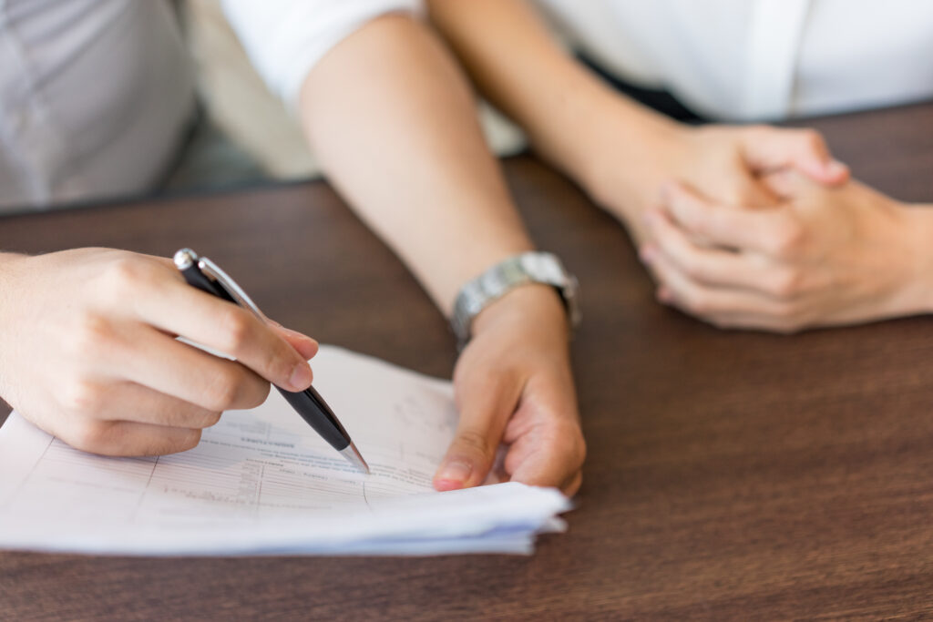 Hands of male agent explaining contract provisions to female client. Close-up of hands of businessman holding document and pointing at it with pen to female colleague at meeting. Consultancy concept